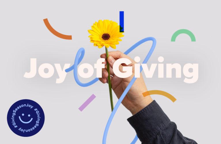 Hand holding up a flower, text says joy of giving